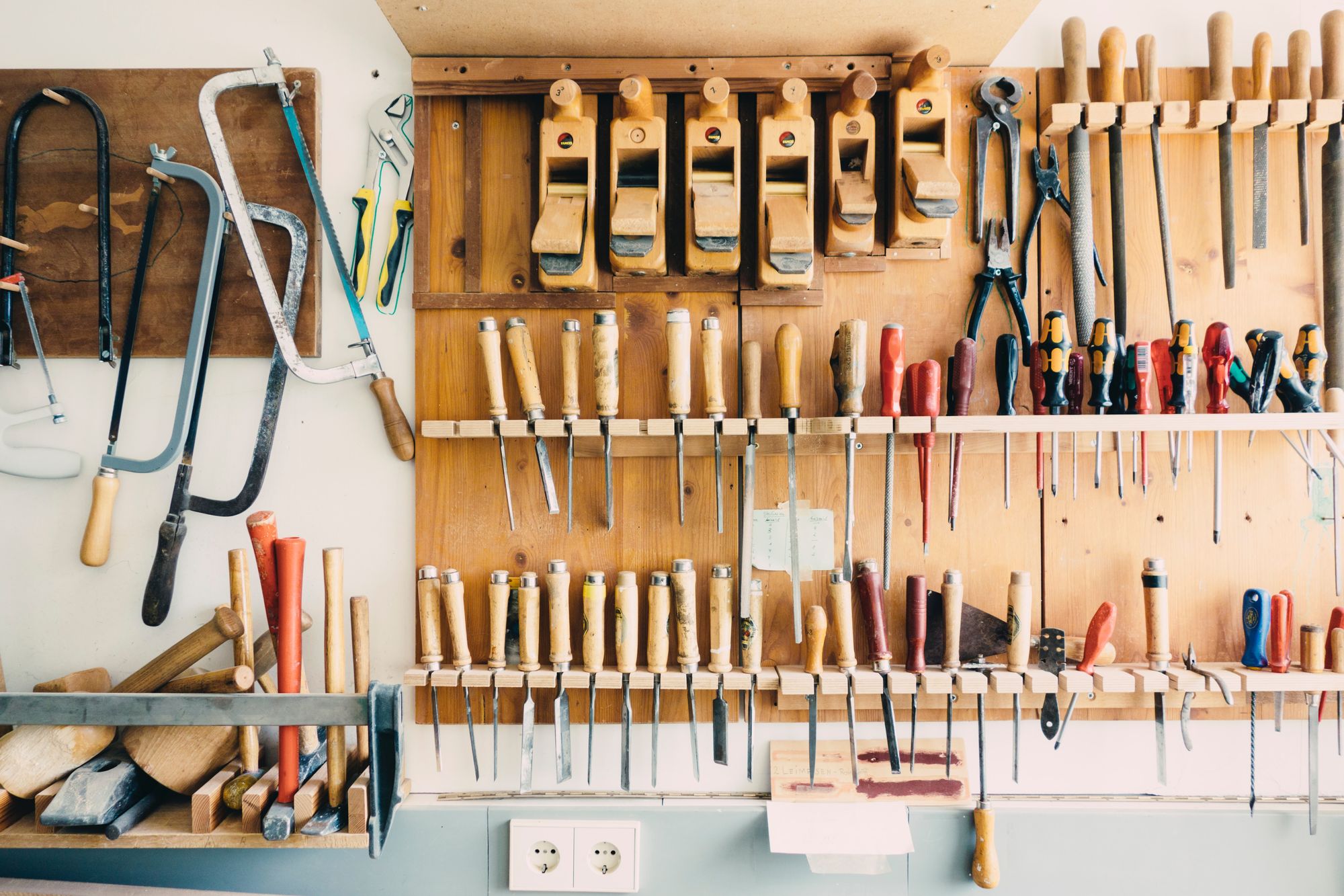 A garage or work space with a bunch of wood-working tools hanging on the wall